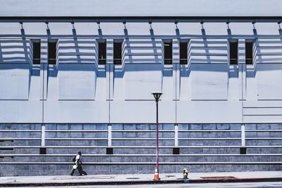 Side view of man walking on footpath by building during sunny day