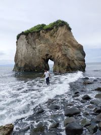 People on rock at beach against sky