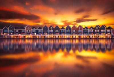 Reflection of buildings on calm lake against orange sky