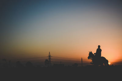 Silhouette man riding horse at desert against sky during sunset