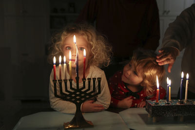 Girls looking at candles while standing with father in darkroom at home