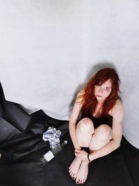 Portrait of beautiful young woman sitting against wall