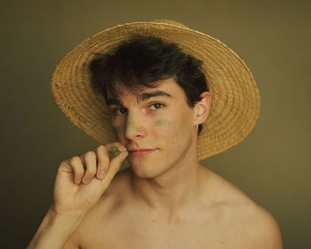 Portrait of shirtless man holding hat against gray background