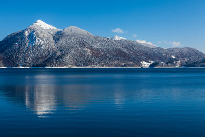 Scenic view of sea and snowcapped mountains against blue sky