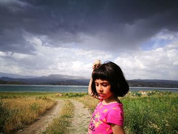 Cute girl standing at lakeshore against sky