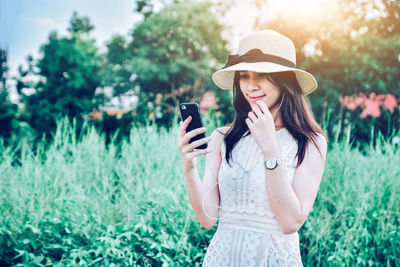 Young woman using mobile phone while standing on plants