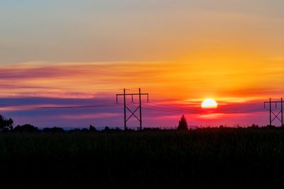 Silhouette electricity pylon on field against sky during sunset