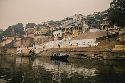 Boats moored in river by buildings against clear sky