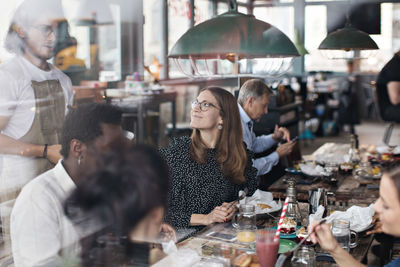 Waiter standing by customers at restaurant seen from window