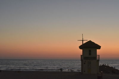 Lighthouse by sea against sky during sunset