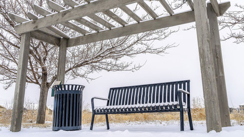 Empty bench by bare tree against sky during winter