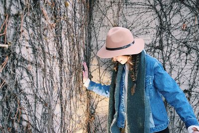 Smiling young woman standing by ivy covered wall