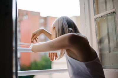 Side view of woman standing by window at home