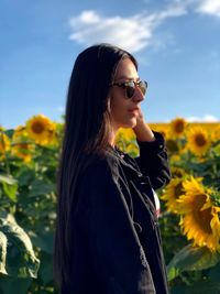 Side view of young woman wearing sunglasses while standing at sunflower farm