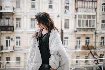 Woman having red wine while wrapped in blanket at balcony