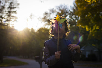 Playful boy blowing pinwheel toy while standing on footpath against sky