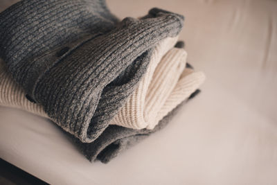 Stack of knitted wool textile sweaters clothes on white blanket in bed at home room close up.