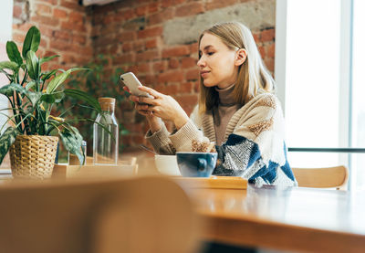 Young woman using phone while sitting on table