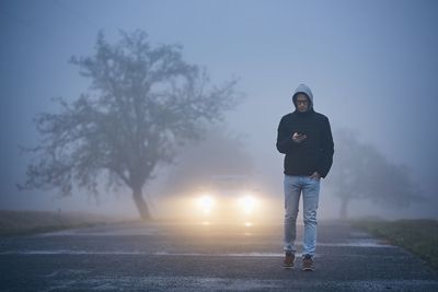Man using phone while walking on road during foggy weather
