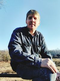 Portrait of young man standing on field against clear sky