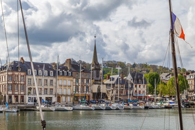 Sailboats moored at harbor by buildings in city against sky