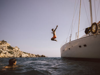 Full length of man jumping from boat into sea against sky