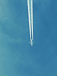 Low angle view of vapor trails in blue sky