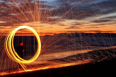 Men spinning wire wool while standing at beach against sky during sunset