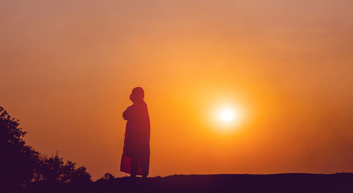 Silhouette man standing against orange sky during sunset