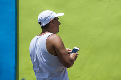 Man holding camera while standing against wall