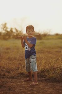 Full length of boy standing on field playing bamboo flute