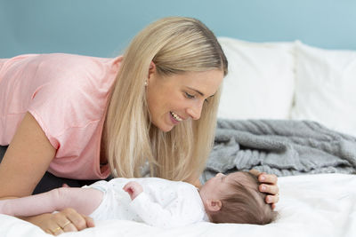 Mother playing with baby girl on bed at home