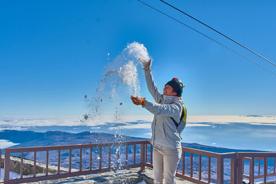 Side view of woman playing with snow on snowcapped mountain