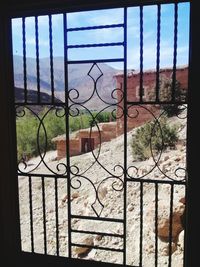 Closed metal gate against sky seen through window