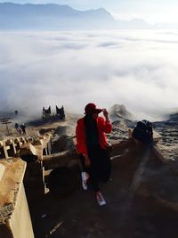 High angle view of mid adult woman sitting on mountain against cloudy sky