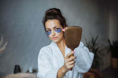 Woman brunette at home in the bathroom applies patches under the eyes, looking in the mirror