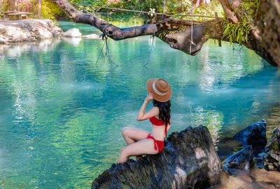 Asian woman in swimsuit sitting on a rock in the blue lagoon near vang vieng, laos