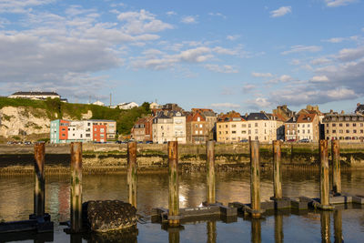 Wooden posts in river against buildings in city