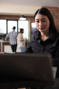 Portrait of young woman using laptop while sitting in office