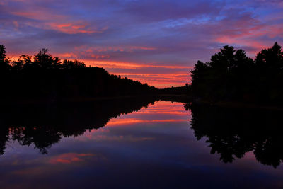 Silhouette trees by lake against sky during sunset