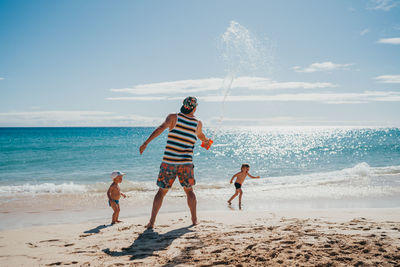 Kids playing with water at the beach with their dad on a sunny day