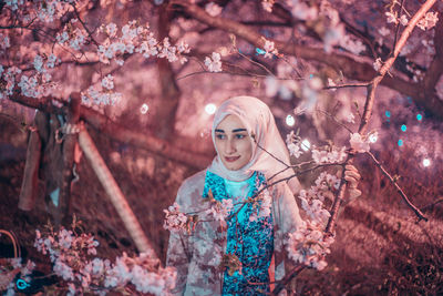 Portrait of young woman standing by cherry tree