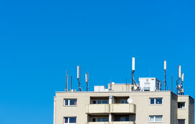 Low angle view of buildings with antennas against clear blue sky