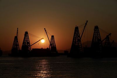 Silhouette cranes at commercial dock against sky during sunset