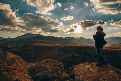 Man standing on rock looking at mountains against sky