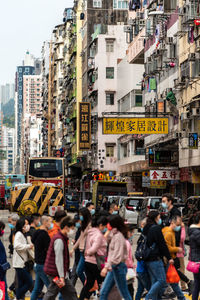 Group of people crossing street in city against buildings and transportations