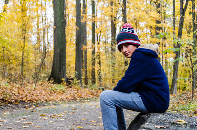 Portrait of smiling boy sitting in forest during autumn