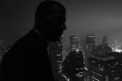Rear view of silhouette man and cityscape against sky at night