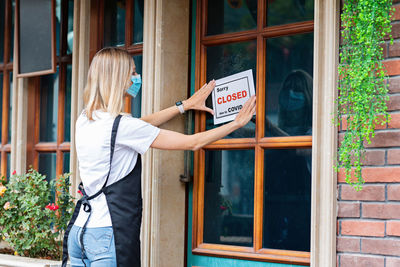 Rear view of woman holding close sign on window