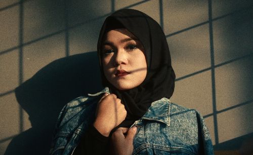 Portrait of young woman wearing hijab against wall during sunset